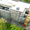 Luftaufnahme einer Baustelle mit Gerüst, Baukran und Rohbau eines mehrstöckigen Gebäudes in der Bauphase